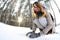 A young and joyful Caucasian girl in a brown coat sculpts a snowball in a snow-covered forest in winter.