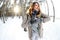 A young and joyful Caucasian girl in a brown coat sculpts a snowball in a snow-covered forest in winter