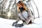 A young and joyful Caucasian girl in a brown coat sculpts a snowball in a snow-covered forest in winter