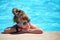 Young joyful child girl resting on swimming pool side with clear blue water on sunny summer day. Tropical vacations