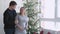 Young joyful family. Husband hugs him pregnant wife near beautiful decorated Christmas tree by the window in studio