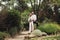 Young joyful groom in shirt embracing pretty smiling bride in white long dress with little bouquet of flowers in hand