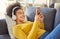 Young joyful mixed race woman wearing headphones and listening to music while typing a message on a phone at home. One