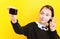 A young joyful schoolgirl girl takes pictures of herself on a small camera on a yellow background. Selective focus