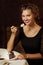 Young joyful woman in black dress happily looking in camera and eating cake