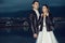 Young just married beautiful stylish couple in black leather jackets standing on the berth in the bay at dusk