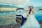 Young just married couple standing near the boat at the seaside in wedding dress and suit.