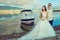 Young just married couple in wedding gown and suit standing near the boat at the seaside looking aside