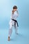 Young karate woman in a white kimono with black belt demonstrates fighting stances and strikes.