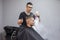 Young Kazakh barber works in a barbershop, a young guy makes a short haircut at a hairdresser, wet his head, water splashes on a