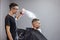 Young Kazakh barber works in a barbershop, a young guy makes a short haircut at a hairdresser, wet his head, water splashes on a