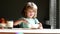 Young kid boy sitting on the table eating healthy food with funny expression on face. Kids eat tasty food and drink milk