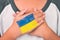 A young kid gripped his chest to pray and the Ukrainian flag painted on the back of his hand