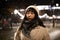 A young Korean Asian woman in a beige coat and hat on a walk through a winter night city, with neon lights, garlands and