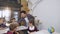 Young Korean teacher walking among between desks puts textbooks on desk while caucasian pupils sitting at the desks