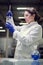 Young lab woman in glasses and white coat with experimental glass in her hands conducts experiments