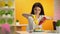 Young lady pouring ketchup and mustard on hot-dog and smiling on camera, canteen