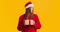 Young lady in Santa hat holding little gift box and looking displeased, pouting lips and shaking head