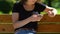 Young lady scrolling social networks on smartphone, relaxing on park bench, app