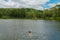 Young lady swimming in a small lake surrounded by green land and wood forest.