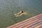 Young lady swimming in a small lake surrounded by green land and wood forest.