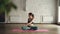 Young lady in trendy sports clothing is doing body twists sitting in lotus position on mat inside yoga studio. Relaxing