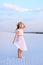 Young lady in white dress and hat going on sand barefoot.