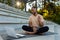 A young Latin American male sportsman, instructor, trainer sits in a stadium on a mat in front of a laptop and teaches