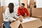 Young latin couple smiling happy unboxing cardboard box at new home