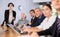 Young Latin female turning on presentation on projector while office coworkers of different ages sitting at table with