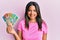 Young latin girl holding australian dollars looking positive and happy standing and smiling with a confident smile showing teeth