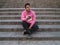 Young latin handsome man sitting on the stairs, looking at his left side with a phone in his hand