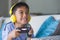 Young Latin little child excited and happy playing video game online with headphones holding controller having fun sitting on couc