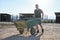 Young latin man carrying a wheelbarrow to pick up horse excrements in stall.