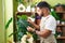 Young latin man florist touching sheet plant at flower shop