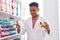 Young latin man pharmacist smiling confident holding pills bottles at pharmacy