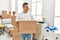 Young latin man smiling happy holding books cardboard box moving at new home