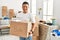 Young latin man smiling happy holding books cardboard box moving at new home