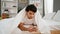 Young latin man using smartphone covering with blanket at bedroom