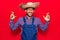 Young latin man wearing farmer hat and apron gesturing finger crossed smiling with hope and eyes closed