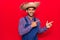 Young latin man wearing farmer hat and apron smiling and looking at the camera pointing with two hands and fingers to the side