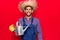 Young latin man wearing farmer hat and gloves holding watering can looking positive and happy standing and smiling with a