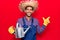 Young latin man wearing farmer hat and gloves holding watering can smiling happy pointing with hand and finger to the side