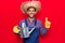 Young latin man wearing farmer hat and gloves holding watering can smiling with an idea or question pointing finger with happy