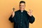 Young latin priest man holding crucifix doing ok sign with fingers, smiling friendly gesturing excellent symbol