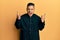 Young latin priest man standing over yellow background shouting with crazy expression doing rock symbol with hands up