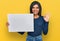 Young latin transsexual transgender woman holding blank empty banner doing ok sign with fingers, smiling friendly gesturing