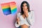 Young latin transsexual transgender woman holding rainbow lgbt flag covering mouth with hand, shocked and afraid for mistake