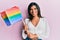 Young latin transsexual transgender woman holding rainbow lgbt flag looking positive and happy standing and smiling with a