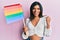 Young latin transsexual transgender woman holding rainbow lgbt flag screaming proud, celebrating victory and success very excited